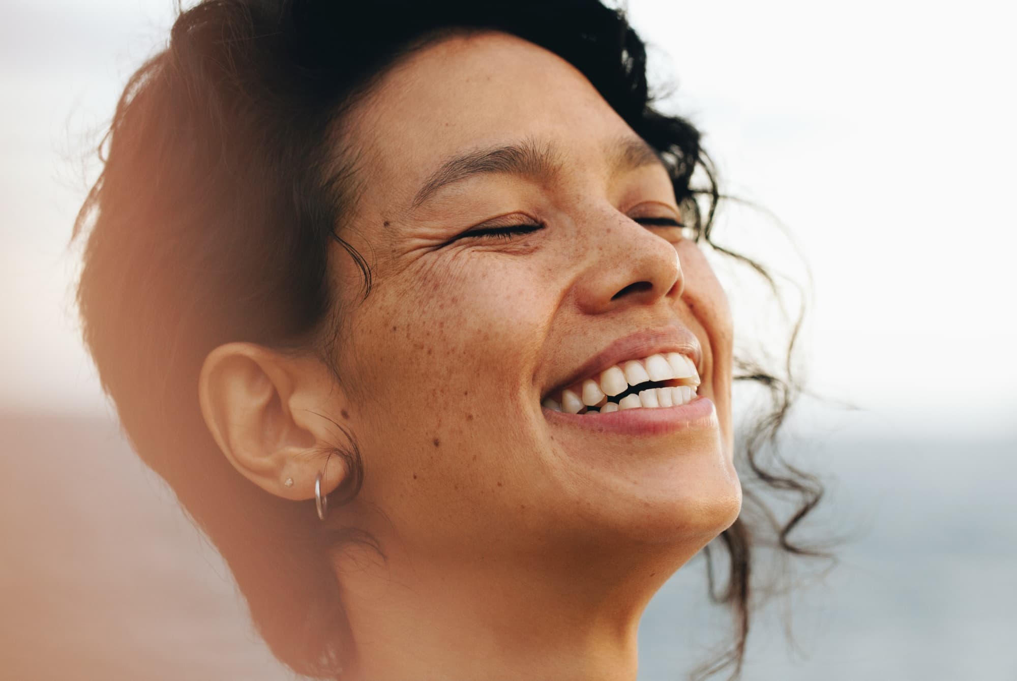 A woman laughing with her eyes closed in warm evening sunlight
