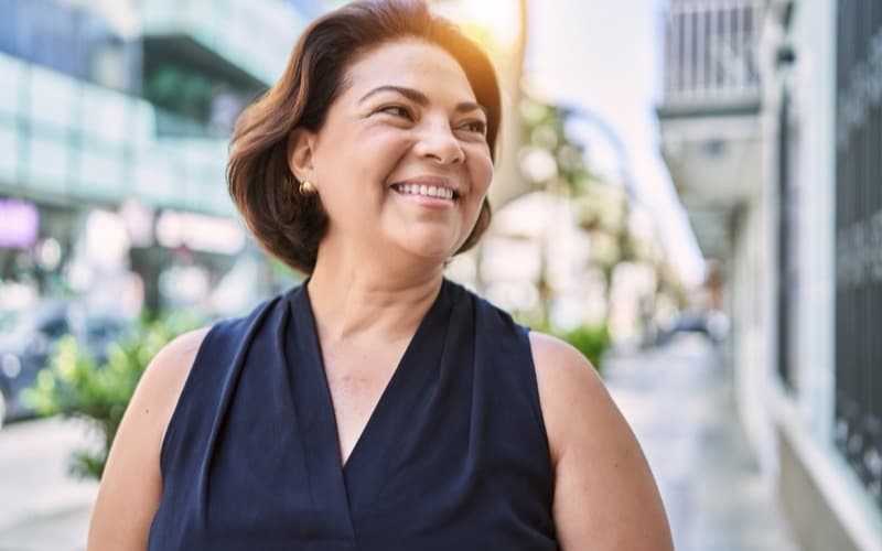 A woman in her forties smiling confidently on a sunlit street