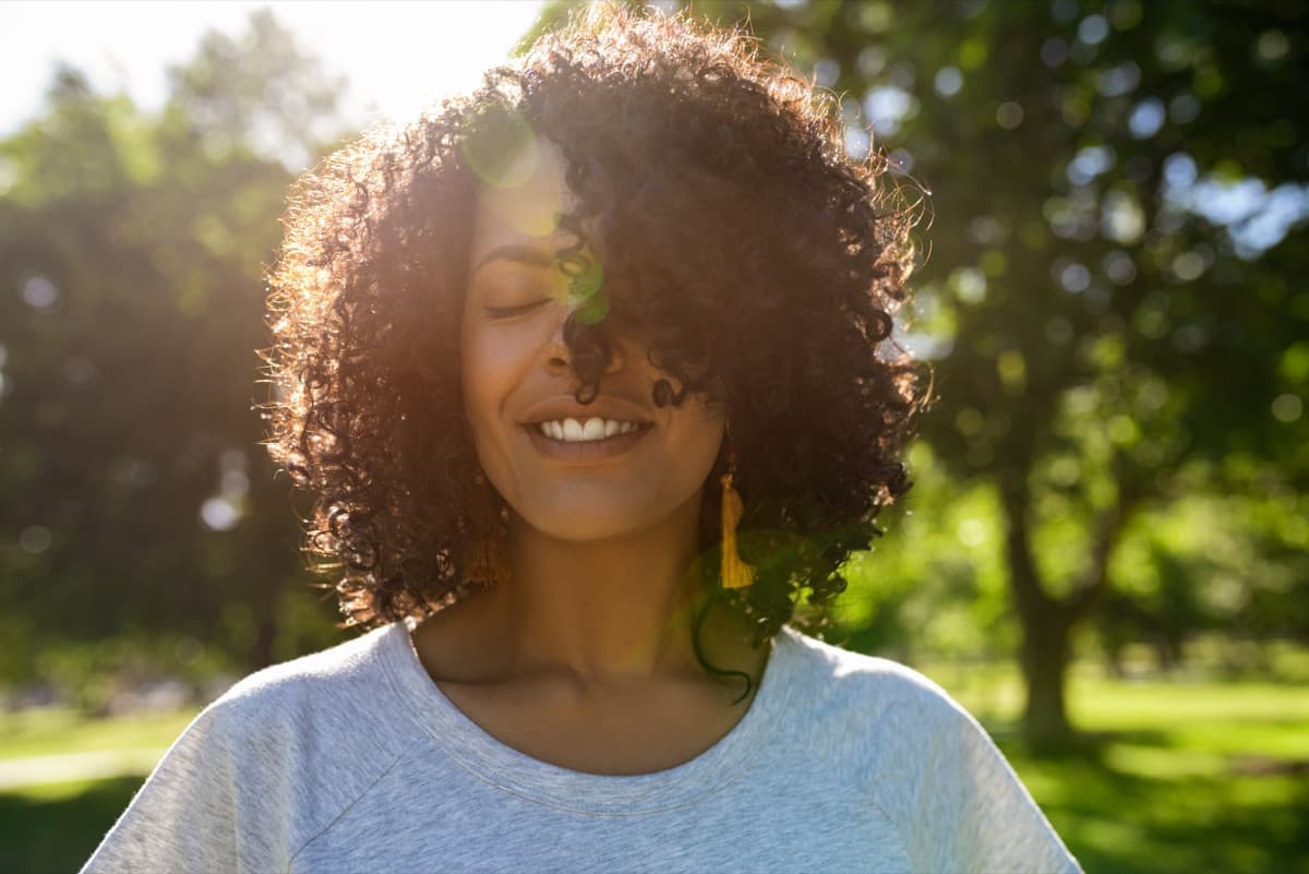 A woman smiling in a sunlit park on a summer afternoon